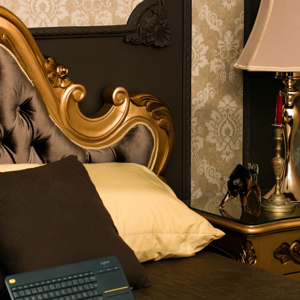 Room de Producciones Olympus, el estudio propio de MVR: cabecero tallado en dorado, papel de colgadura damasco, lámpara de mesa encendida y teclado inalámbrico listo sobre la cama